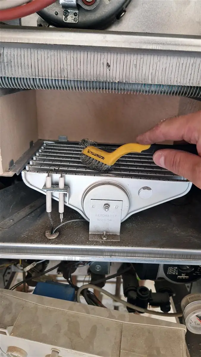 Technician using a brush to clean the burners component inside a gas boiler during maintenance.